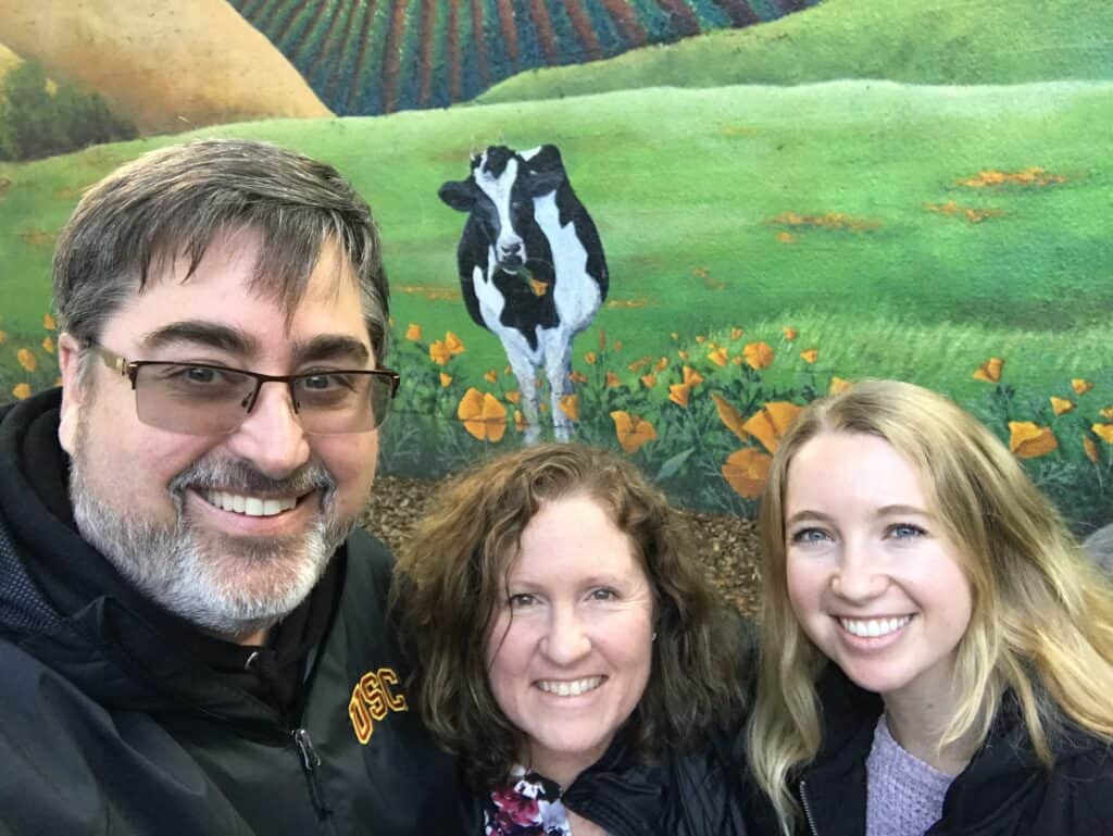 Sabrina Panfil and her parents in front of a mural with a cow