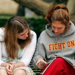 Students reading a book on a park bench wearing Fight On sweater