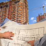 Engineers with building plans at high-rise construction site, close-up