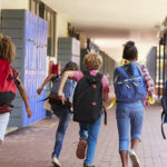 School kids running in elementary school hallway, back view