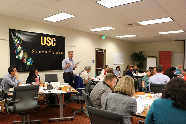 Presenter standing in front of a black and gold USC Price Sacramento banner in a classroom.
