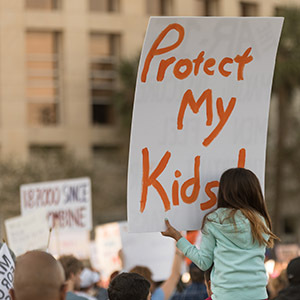 Child on Parents Shoulders Holding a Protest Sign