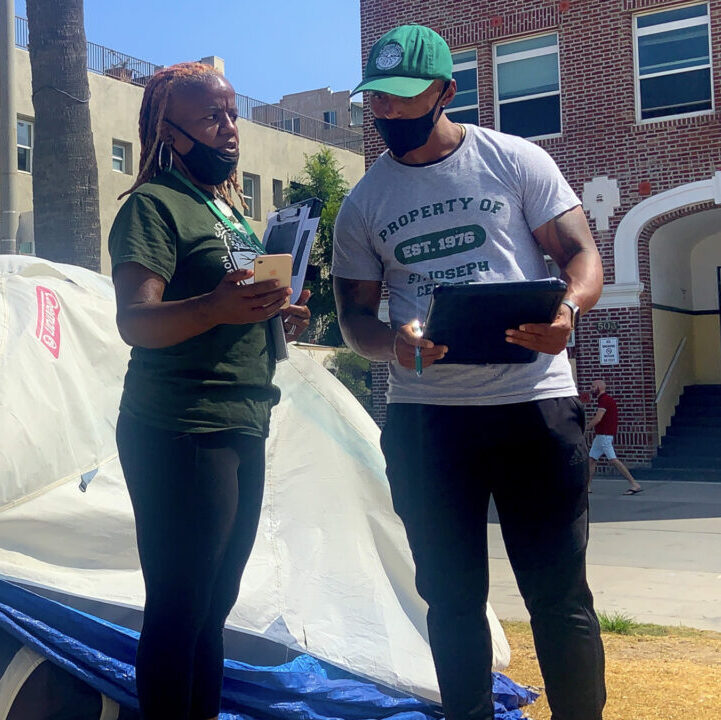 Two homelessness outreach staffers stand in front of a tent