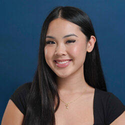 Nina Nguyen smiles in this headshot of her in front of a blue bakcground