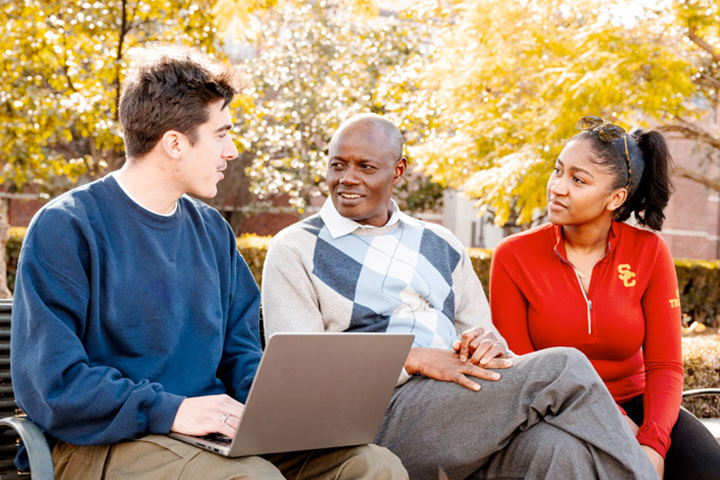 Moussa Diop sits on a bench with two USC students