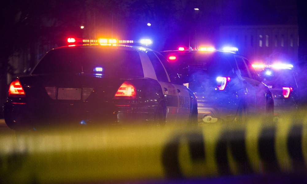 Police cars with their lights on are parked at night near yellow caution tape