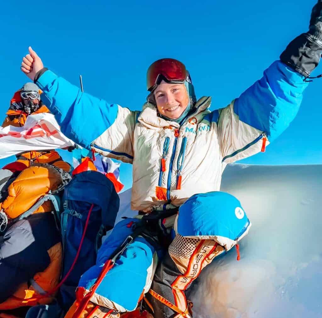 Lucy Westlake sits at the summit of Mount Everest with with arms raised.