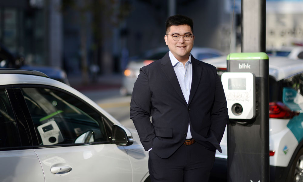 Dylan Di poses by an EV charging station