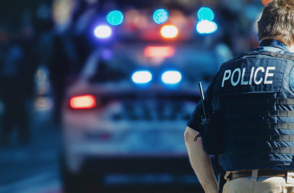 A police car with a police officer standing with his back towards the camera.