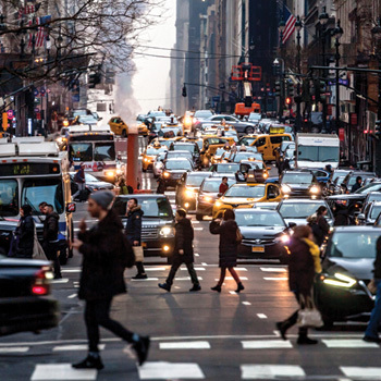 Man walks across the street with a lot of traffic behind him in Manhattan