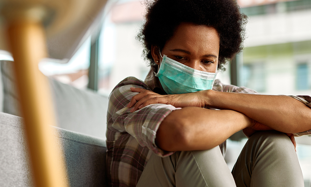 Sad woman wearing a face mask sitting at home and thinking about something.