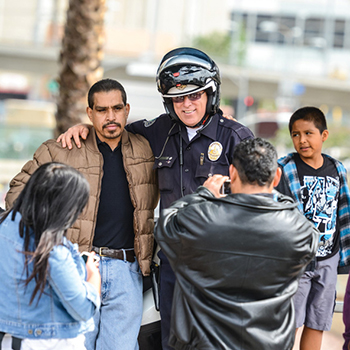 Photo of a LAPD policeman with his arm around a man, smiling for a photograph.