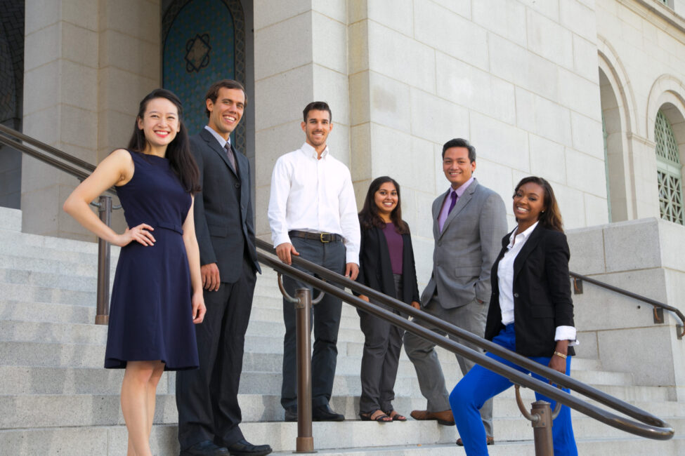 MPA students in professional clothes standing on stairs in front of a public administration building.