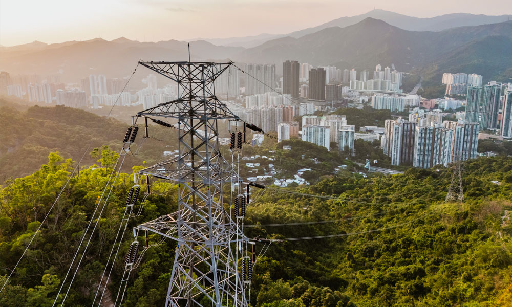 High voltage power line polls are seen on a hill overlooking a city.
