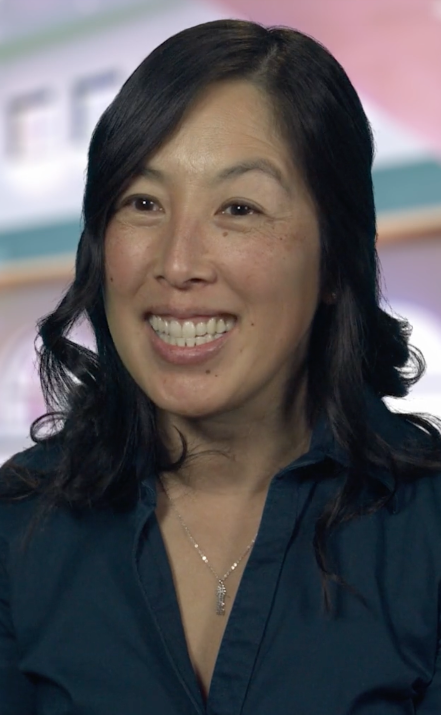 Woman wearing a navy collared shirt and silver necklace smiling.
